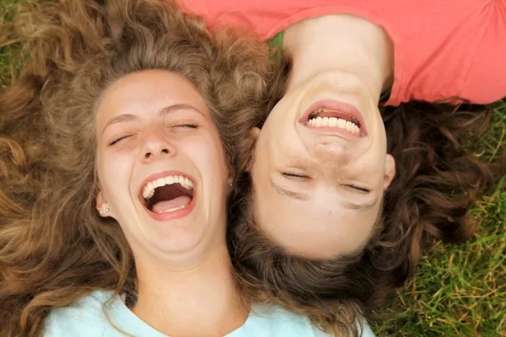 Two women laying down with their heads facing different ways laughing