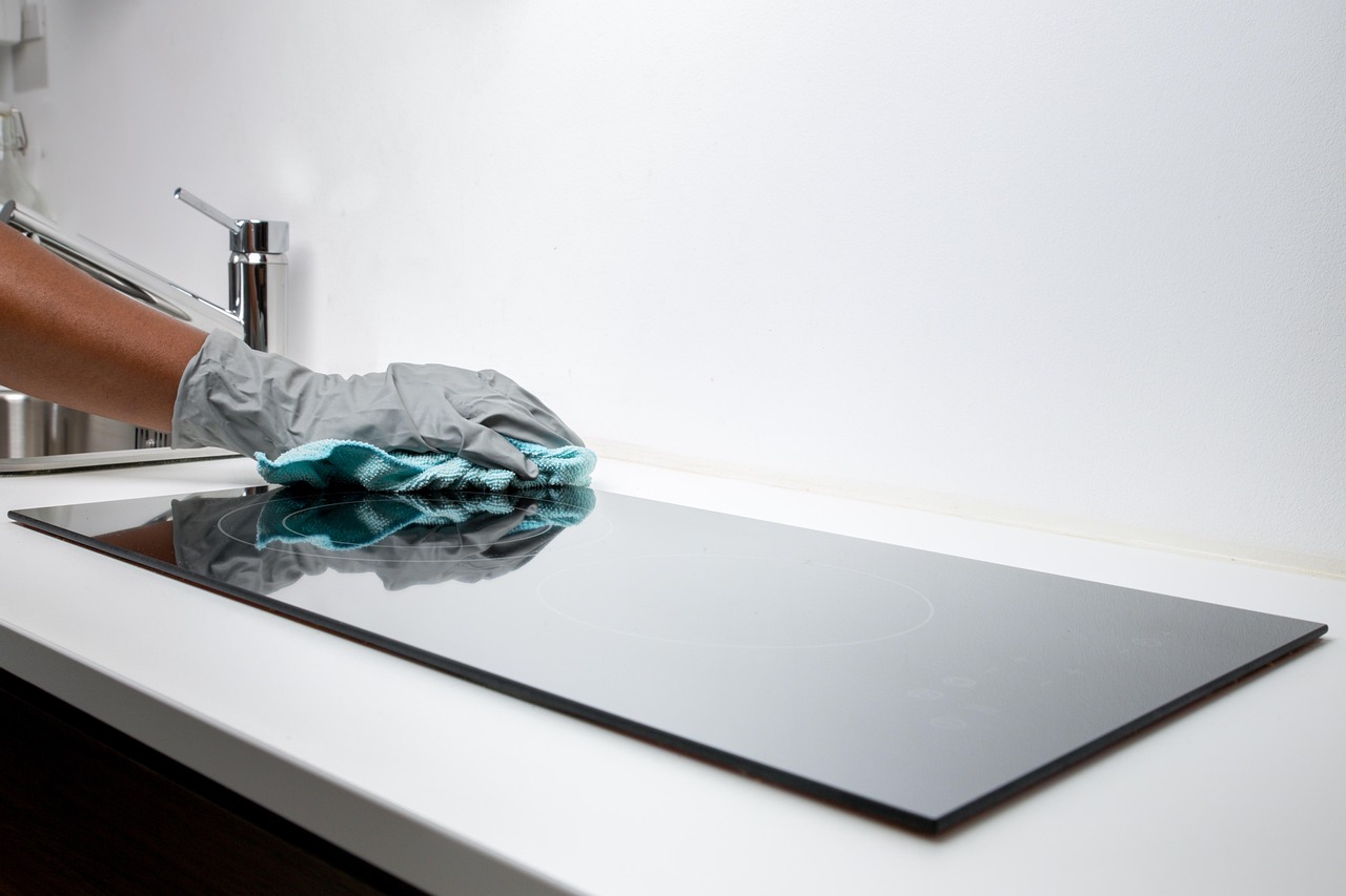 A person wiping down a glass top stove as part of their summer cleaning hacks